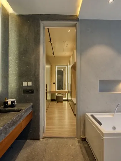 A master bathroom featuring a dark stone countertop and sink, a large jacuzzi tub, and limewash-textured walls. A doorway provides a glimpse into the adjoining walk-in closet.
