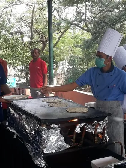 A chef serving a freshly made dosa from a live counter at an outdoor event. Live stations like these are a great way to offer hot, customized food and entertain guests at the same time.