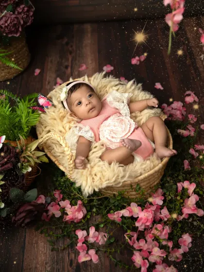 A little princess in her enchanted garden. This setup features a baby girl in a pink floral outfit, lying in a soft basket surrounded by flowers and greenery.