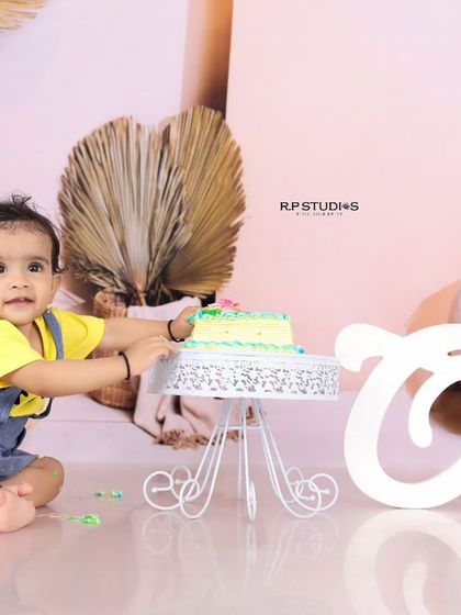 A little girl reaches for her first birthday cake in a beautiful boho-chic setup. The pastel pink and earth-toned balloons create a soft and modern aesthetic for her celebration.