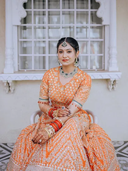 A seated portrait of the bride, showcasing her full lehenga and the intricate details of her jewelry.