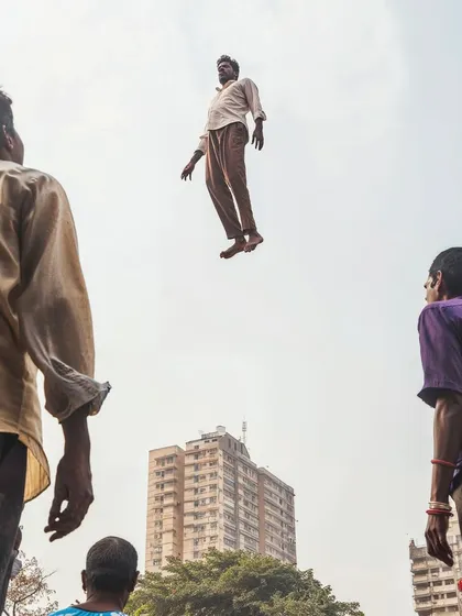 A man levitates above the ground in Mumbai, observed by onlookers. This series, 'a moment of lightness', introduces a touch of the magical and surreal into the dense reality of the city.