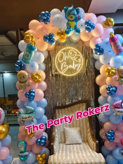 A classic "Oh Baby" themed baby shower decoration. This setup includes a pink and blue balloon arch with baby-themed foils and a neon sign.