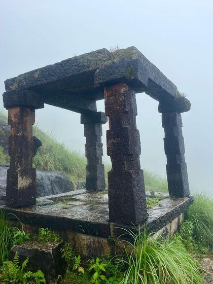 The historic Kallu Mantapa on the Kumara Parvatha trail, a stone structure that serves as a resting point for trekkers amidst the misty landscape.