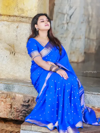 A vibrant blue saree stands out against the neutral tones of the ancient stone pillars. The bride's relaxed pose creates a beautiful and serene image.