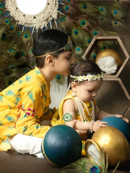 A tender moment between siblings during a Janmashtami shoot. An older brother gives his baby sister a gentle kiss on the forehead.