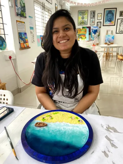A participant smiling with her completed resin beach art. The vibrant colors and glossy finish make it a real statement piece.