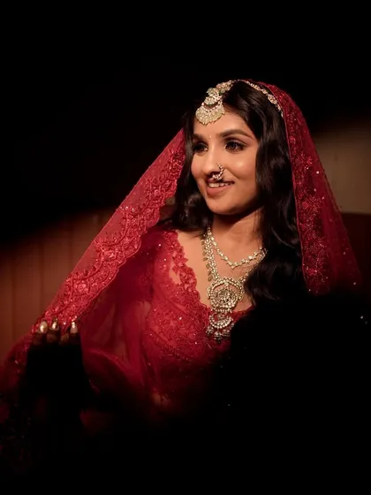 A dramatic and beautiful shot of the bride under her red veil. The lighting highlights her glowing skin and defined eyes, creating a timeless and artistic bridal portrait.