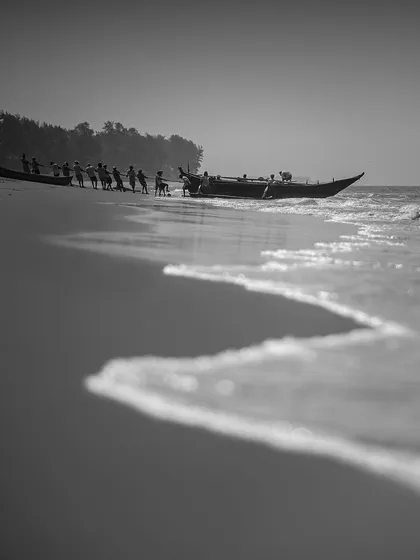 A group of fishermen works together to pull their boat ashore. The low angle and the line of the wave create a dynamic composition, telling a story of hard work and community.