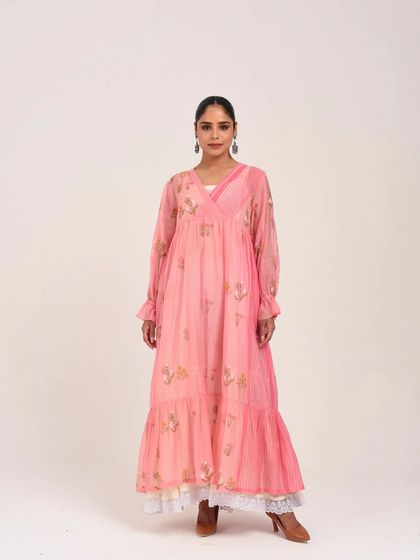 A model in a soft pink tiered dress with long sleeves and delicate floral embroidery, exuding a romantic, bohemian charm.