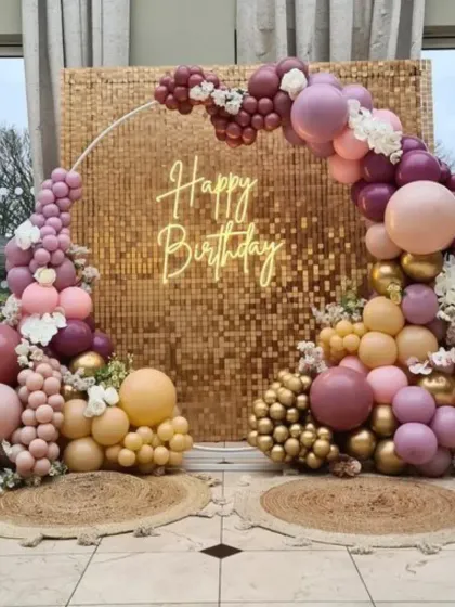 A beautiful birthday setup with a rose gold sequin wall. The organic balloon arch in dusty rose, beige, and gold creates a warm and trendy aesthetic.