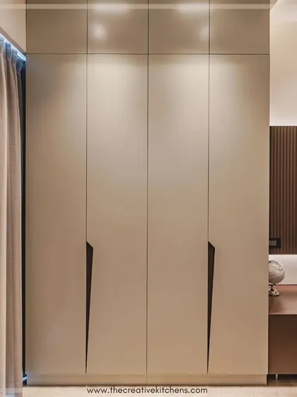 A sleek and bespoke wardrobe with long, sturdy doors finished in a crisp matte lacquer. The recessed, angular designer handles create a stark geometric contrast, making a strong statement through subtlety.