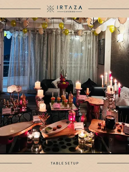 A beautifully styled table for an indoor party. The setup makes use of vertical space with tiered platters and is decorated with candles and balloons, creating a festive and abundant feel.
