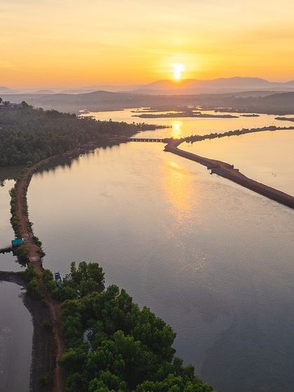 A peaceful sunset over the backwaters of coastal Karnataka. The still water perfectly reflects the colorful sky, creating a symmetrical and tranquil scene.