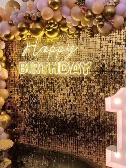 A first birthday party with a touch of glamour. The gold sequin wall provides a sparkling background for the peach and gold balloon arch and the light-up number '1'.