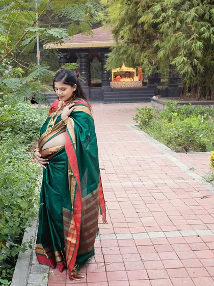 A beautiful profile shot of the expectant mother cradling her bump. Dressed in a traditional silk saree, she walks through a garden path, embodying grace and the beauty of new life.
