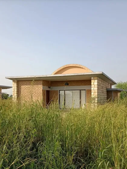 A cottage at Waghoba Ecolodge surrounded by tall, wild grasses. We sited each cottage carefully to provide a private, immersive forest living experience, using passive strategies like thick adobe walls and vaulted roofs to keep the interiors cool.