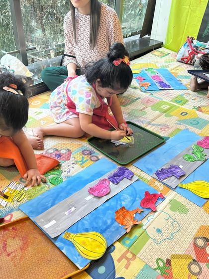 A focused artist at work during our transport-themed class. Using individual trays helps children concentrate on their own creations while still being part of a group activity.
