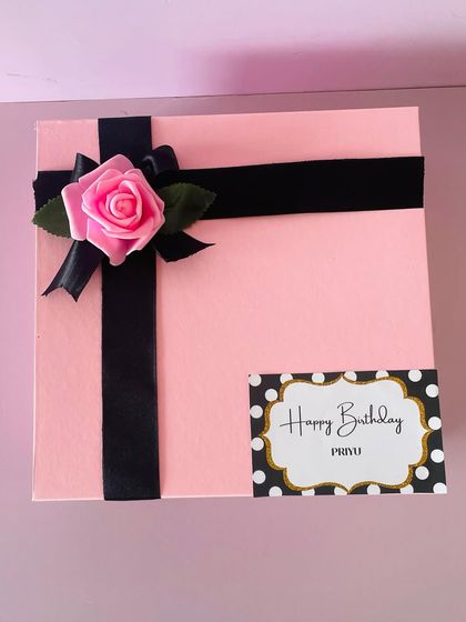 The exterior of a personalized birthday hamper. This pink box is elegantly wrapped with a black ribbon and a custom "Happy Birthday" tag.