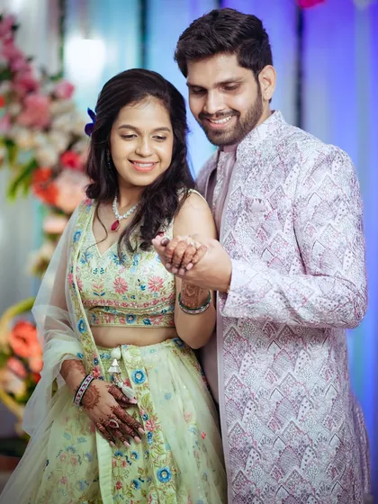 A candid shot of the newly engaged couple sharing a happy moment. The groom holds the bride's hand, and their smiles show their genuine excitement and affection.