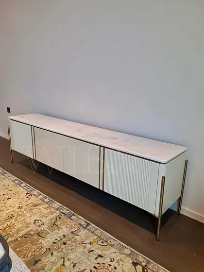A different view of the white TV console, highlighting the contrast between the textured fluted doors and the high-gloss plain doors, all tied together with subtle gold metal inlay.