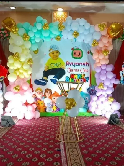 A Cocomelon-themed first birthday stage decoration with a custom backdrop and balloon arches in pastel shades.