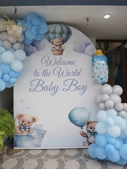 A beautiful 'Welcome to the World Baby Boy' backdrop with a hot air balloon and teddy bear theme, framed by a soft blue and grey balloon garland.