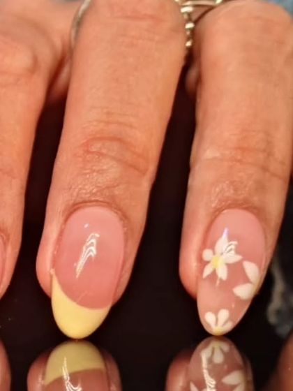 A close-up of the yellow-tipped French manicure, detailing the hand-painted white flower on an accent nail.