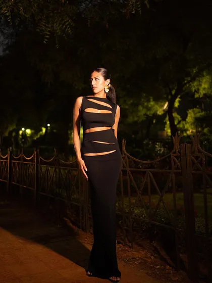 A classic fashion pose against a dark, natural background. The lighting is carefully controlled to make the model and her outfit the central focus, creating a timeless and elegant image.