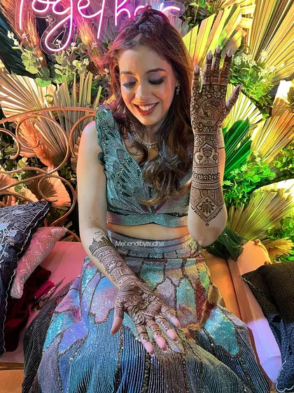 A happy bride showing off her designer mehendi, which features modern, spaced-out motifs on the arms.