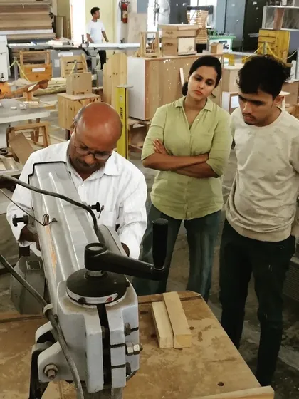 An instructor demonstrates the use of a scroll saw, used for cutting intricate curves and patterns, as two students observe closely.