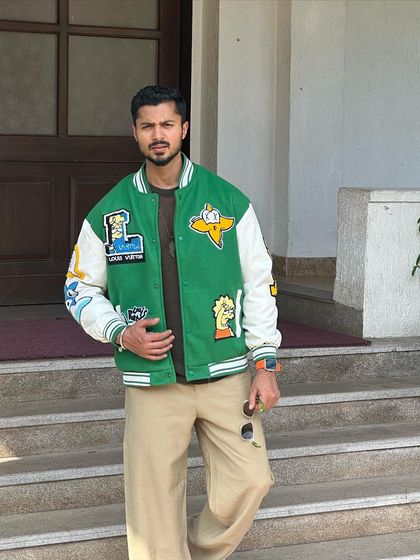 A three-quarter shot of the green varsity jacket, showing how it pairs with casual trousers.