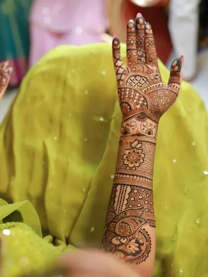 A professional shot of a bride's mehndi day, showcasing the intricate details of the peacock and floral patterns on her arm.