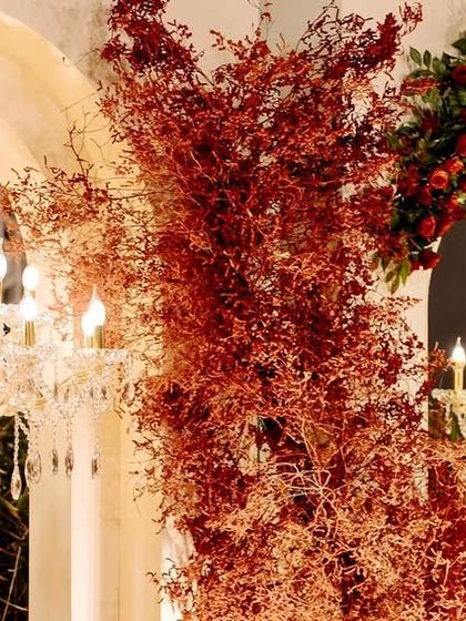 A close-up of the dramatic reception decor, showing the contrast between the delicate crystal chandeliers and the bold, fiery red foliage.