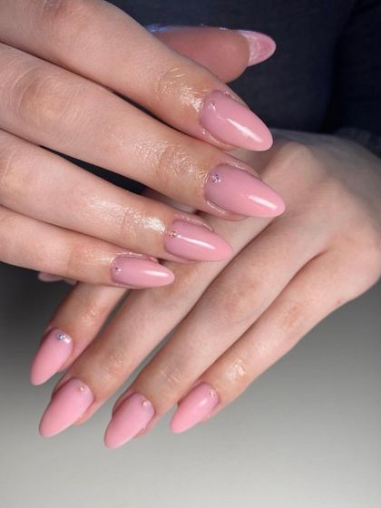 A soft pink manicure on stiletto-shaped nails, with a tiny rhinestone placed at the cuticle for a subtle touch of sparkle.