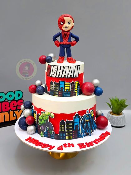 A two-tier Spiderman cake for a 4th birthday, featuring a custom figurine of the birthday boy as Spidey, alongside other superhero elements.