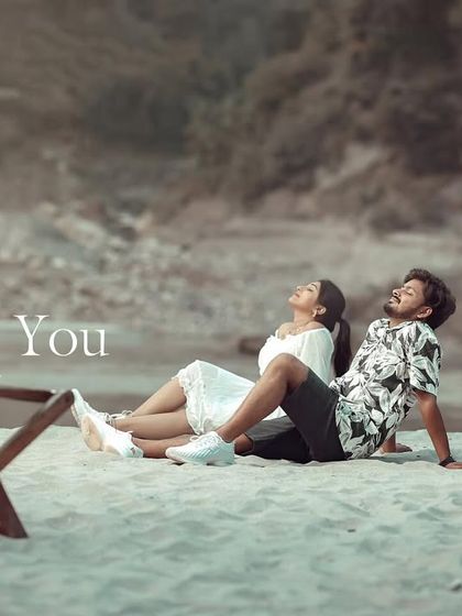 A relaxed shot of the couple chilling on the sand between two wooden chairs. This has a very casual, "day at the beach" vibe.