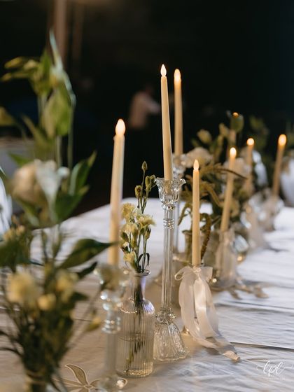 A detail of the candlelit tablescape, with delicate white ribbons tied to the candle holders. These small touches add to the romantic and personalized feel of the event.
