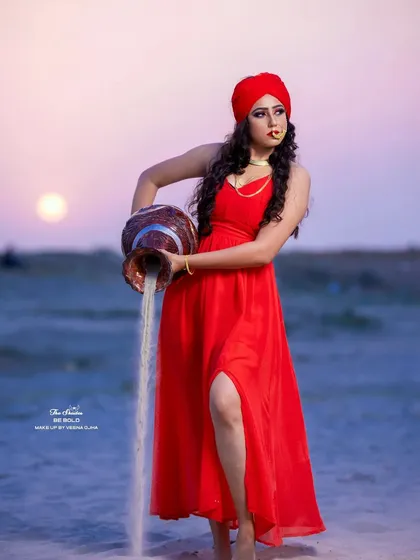 An artistic shot from a conceptual shoot on the sands. The vibrant red dress and turban are contrasted with dramatic eye makeup and a traditional nose ring, creating a powerful and story-driven visual.