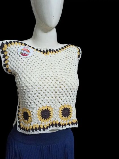 Inspired by sunflowers, this sleeveless top features a line of sunflower granny squares along the bottom. The simple white top with a pop of yellow and brown makes it a cheerful and fun piece to wear.