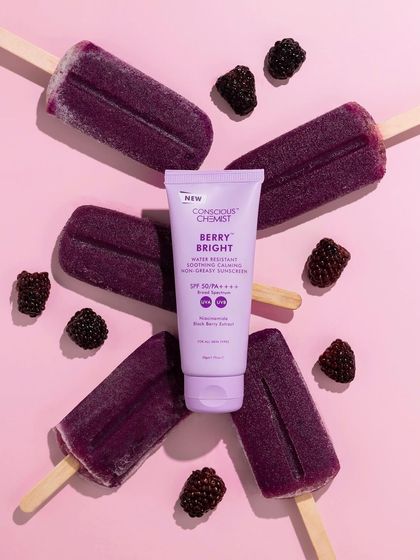 A fun, summery flatlay featuring berry-flavored sunscreen surrounded by real blackberries and popsicles. This creative styling makes the product look delicious and refreshing.