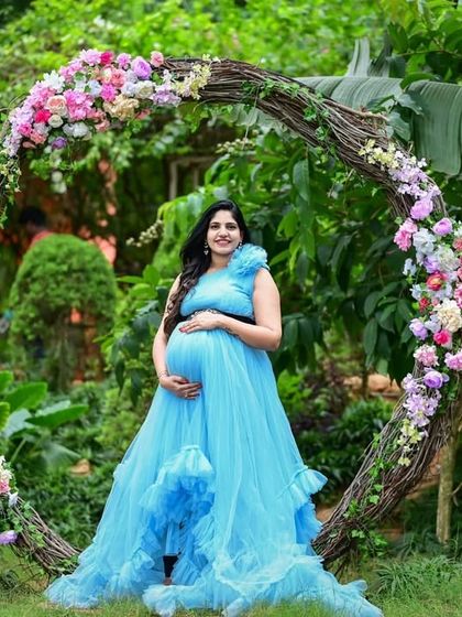 A beautiful maternity portrait in a garden. This client is wearing my sky blue ruffled gown, sitting in a circular floral archway for a perfect photo.