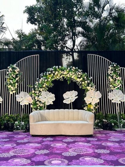 A modern and stylish stage design featuring a black backdrop with white geometric panels. A floral arch and illuminated flower props add a touch of softness and light to the contemporary setup.