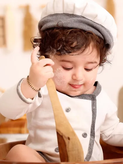 A close-up of the little chef, focused intently on his wooden spoon. This detailed shot highlights his adorable expression and the charming costume.