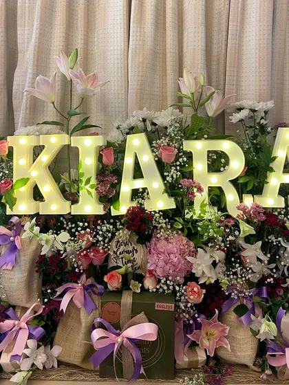 Celebrating a birthday should be as unique as the person themselves. This stunning floral hamper, personalized with the name 'Kiara' in glowing marquee letters, is designed to be an unforgettable centerpiece for any celebration.