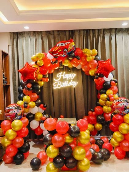 A dynamic Disney Cars themed birthday party decoration. This setup features a full ring of red, black, gold, and white balloons, with Lightning McQueen foil balloons and a central neon sign, creating an exciting photo backdrop.