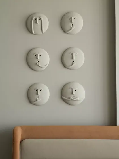 A bed wall panel detail featuring white sculptural faces with various quirky expressions. The concept behind these faces symbolizes the spectrum of human emotions, perfect for adding personality to minimalist interiors.