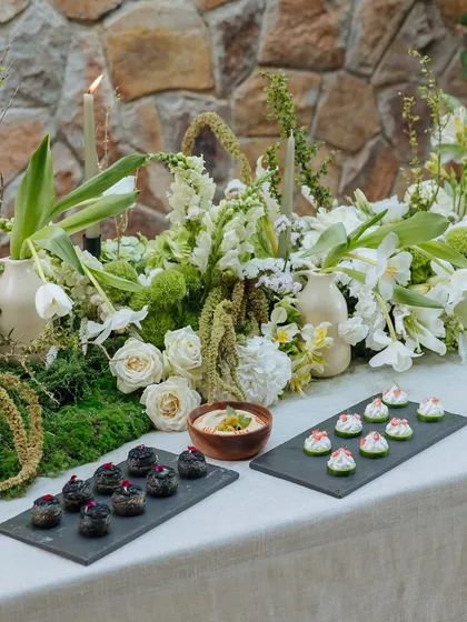 Savory bites are presented on modern slate trays, contrasting with the organic, flowing centerpiece of the Earth Table. This shows our blend of contemporary style and natural beauty.