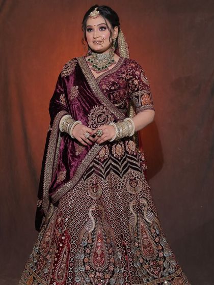 A full view of a bride wearing a heavily embroidered wine-colored velvet lehenga. This outfit is synonymous with luxury and is a top rental for winter bridal shoots.