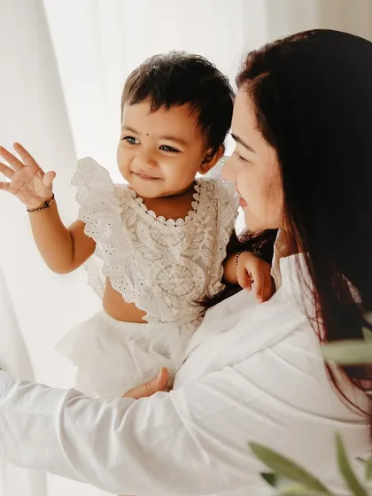 A mother holds her one-year-old, both looking out the window. This candid, lifestyle portrait captures a simple, beautiful moment of their day together.